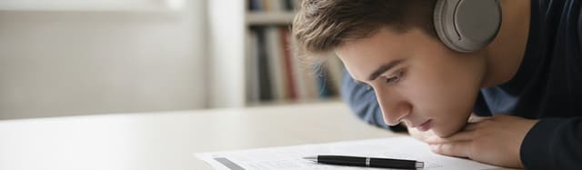 un candidat au casque audio devant une feuille de questions à choix multiples et un stylo, sur une table claire, ambianc