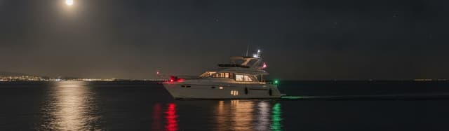 un bateau de plaisance à moteur de nuit montrant ses feux de côté (rouge/vert) sur une mer calme, sans marque commercial