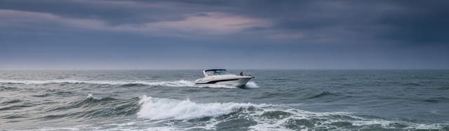 un bateau de plaisance à moteur au large sous un ciel de mer se couvrant, houle modérée moutonnant, ambiance avant grain