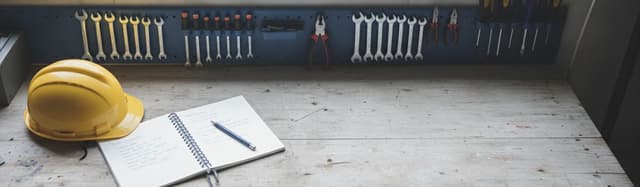 établi d'atelier vu de dessus avec outils rangés, carnet de liaison ouvert et casque de chantier posé à côté, lumière na