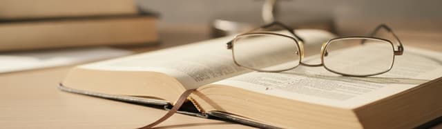 un dictionnaire ouvert sur une page de la lettre V, une paire de lunettes de lecture posée en travers et un marque-page,