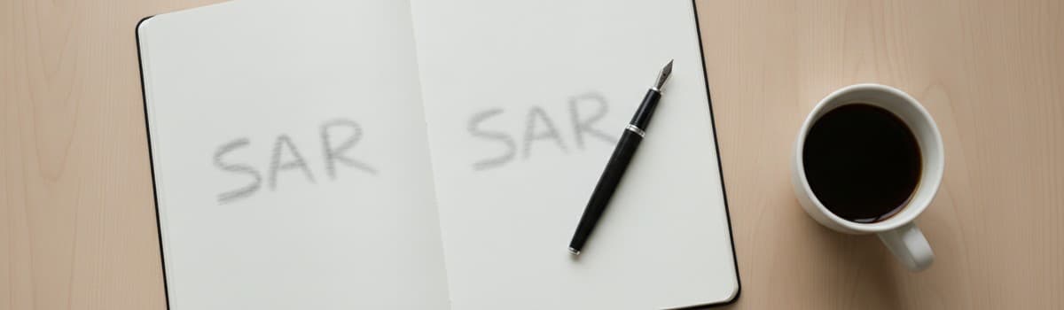 un bureau clair vu de dessus avec un carnet ouvert, un stylo plume posé en diagonale et une tasse de café, deux mots man