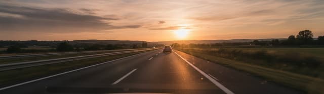 Vue depuis le pare-brise d'une voiture sur une autoroute en fin de journée, un véhicule circulant devant à faible distance