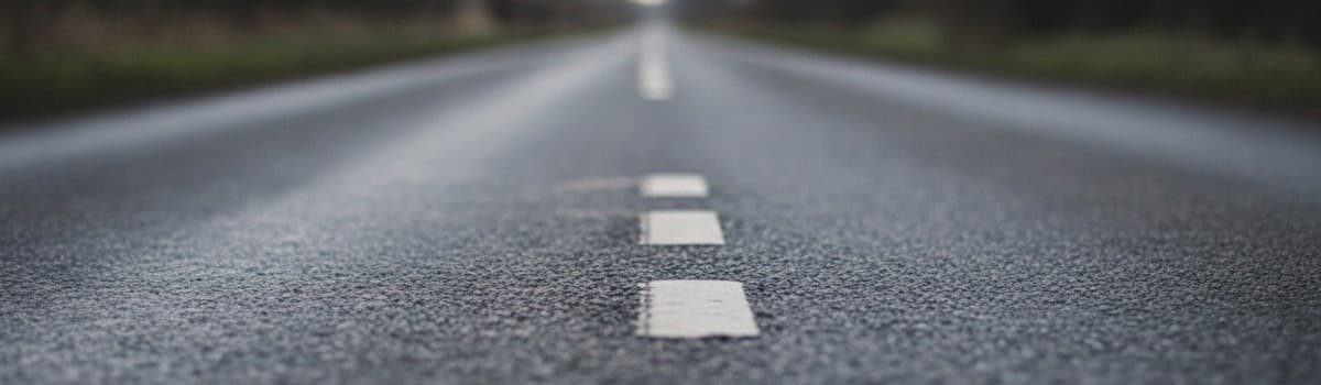 vue rasante et légèrement plongeante d'une route de campagne étroite en fin de journée, chaussée sans marquage central,