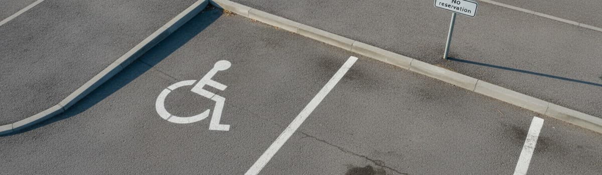 place de stationnement réservée vue en plongée légère, pictogramme fauteuil roulant blanc peint au sol, panneau d'interd