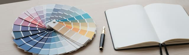 un nuancier de peinture déployé en éventail sur un bureau en bois clair, à côté d'un stylo plume et d'un carnet ouvert,