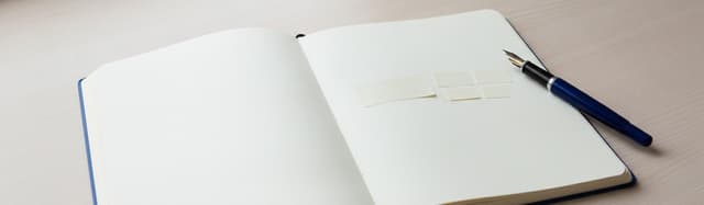 un cahier ouvert avec deux petites étiquettes de papier posées côte à côte sur la page, l'une courte, l'autre découpée e