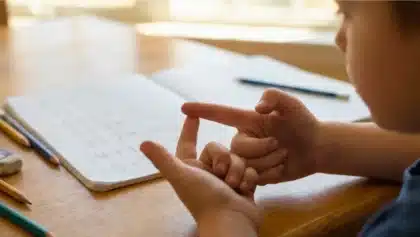 Un jeune enfant compte sur ses doigts pour résoudre un calcul d'addition